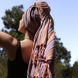 May include: A woman with a striped scarf wrapped around her head, standing outdoors with a blue sky in the background.