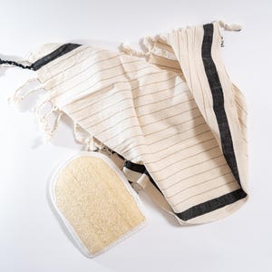 May include: A white and black striped towel with fringe edges and a natural loofah sponge.