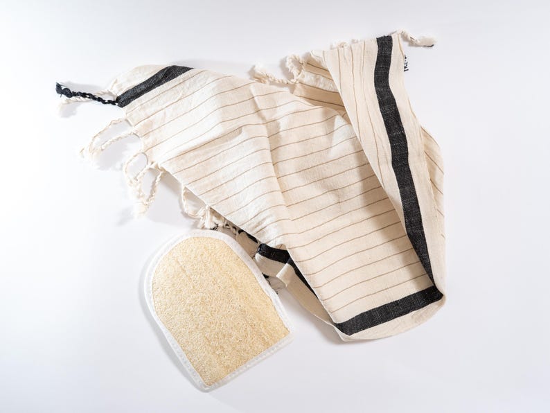 May include: A white and black striped towel with fringe edges and a natural loofah sponge.