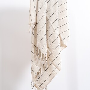 May include: A cream-colored throw blanket with black stripes and fringe. The blanket is folded and hanging from a white rod.