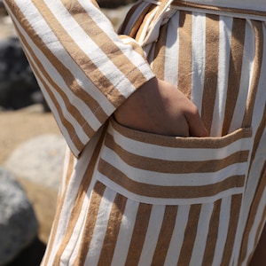 May include: A long, striped robe with a brown and white pattern. The robe has a sash tie and a patch pocket on the front.