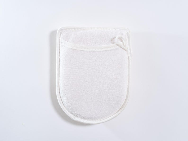Op de afbeelding: Witte badhandschoen van badstof met een lus om op te hangen. De handschoen is ontworpen om de huid te exfoli&euml;ren en te reinigen.