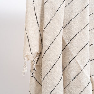 May include: A cream-colored throw blanket with black stripes and fringe. The blanket is folded and draped over a white rod.