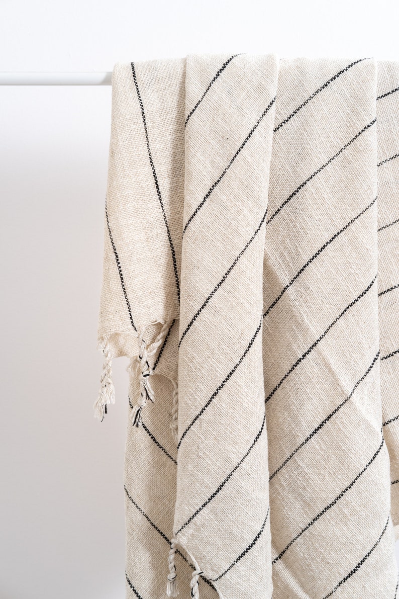 May include: A cream-colored throw blanket with black stripes and fringe. The blanket is folded and draped over a white rod.