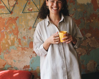 May include: A person wearing a striped, light gray shirt and matching shorts, smiling and holding a yellow mug.