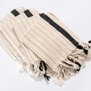 May include: A set of four striped towels with black trim and fringe. The towels are folded and stacked on a white surface.