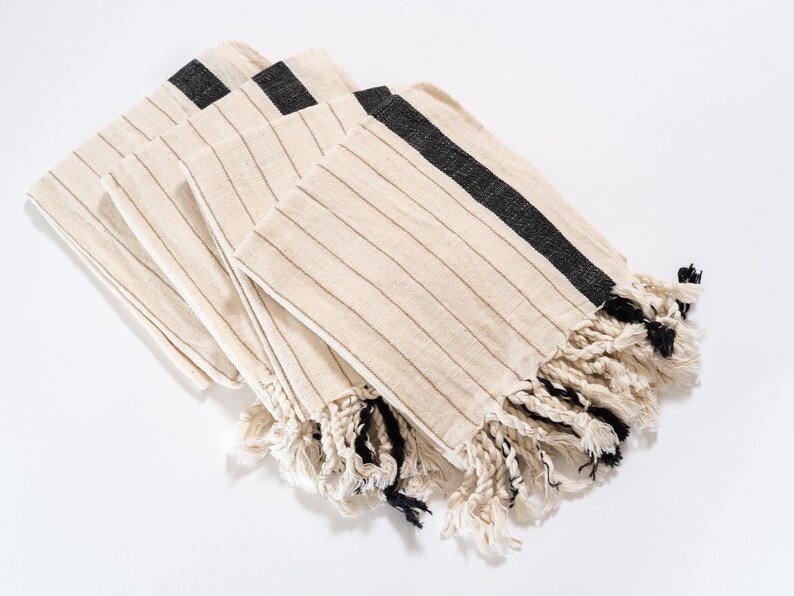 May include: A set of four striped towels with black trim and fringe. The towels are folded and stacked on a white surface.