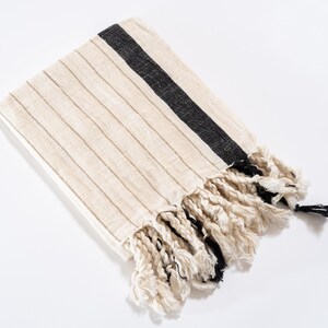 May include: A white and black striped throw blanket with fringe. The blanket has a black stripe running diagonally across the fabric.