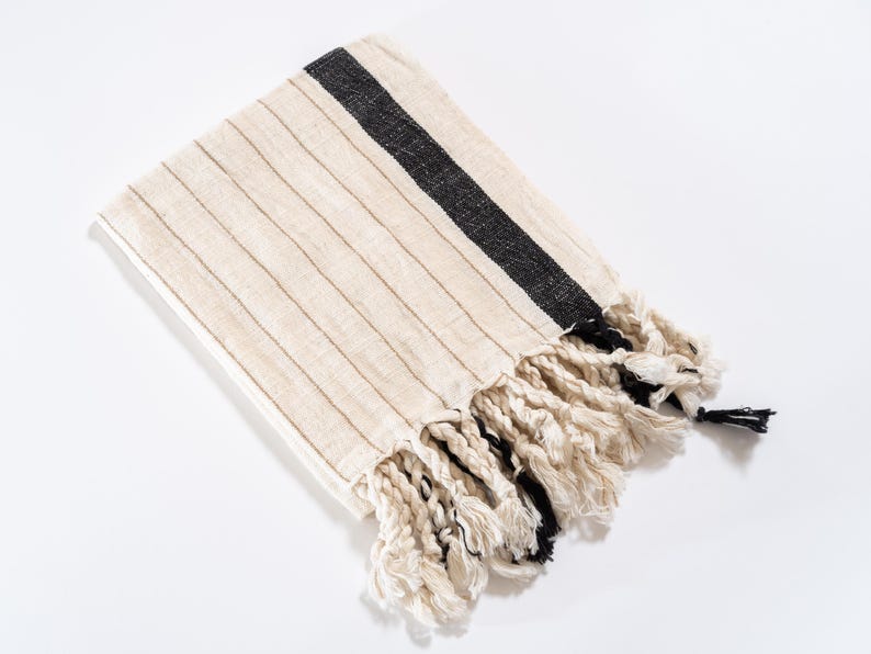 May include: A white and black striped throw blanket with fringe. The blanket has a black stripe running diagonally across the fabric.
