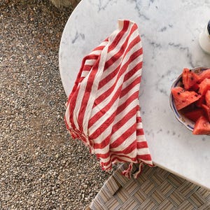 Peut inclure: Serviette de cuisine en coton ray&eacute;e rouge et blanche avec des franges accroch&eacute;e &agrave; une table en marbre blanc avec une assiette de tranches de past&egrave;que.