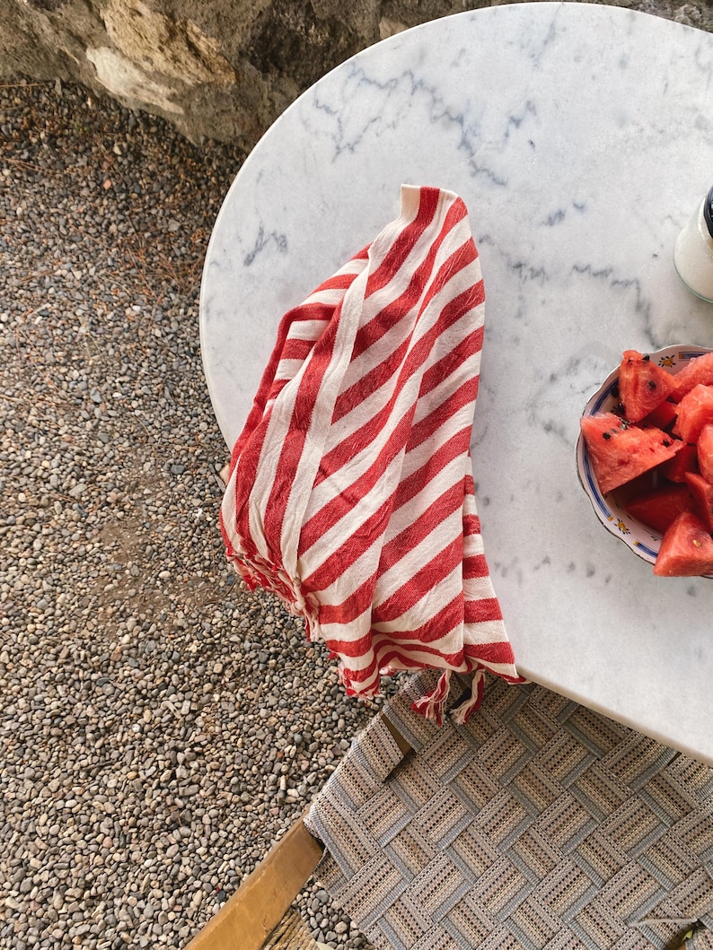 Peut inclure: Serviette de cuisine en coton ray&eacute;e rouge et blanche avec des franges accroch&eacute;e &agrave; une table en marbre blanc avec une assiette de tranches de past&egrave;que.