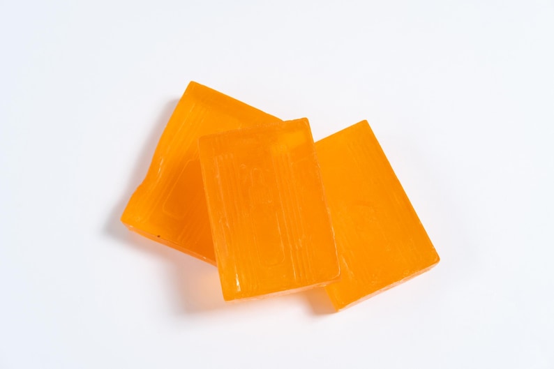 May include: Three rectangular bars of translucent orange soap arranged in a slightly overlapping cluster. Each bar features a smooth, glossy surface with subtle vertical lines embossed into the material, creating a uniform appearance across all pieces.