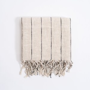 May include: A cream-colored striped throw blanket with black stripes and fringe on the bottom edge.