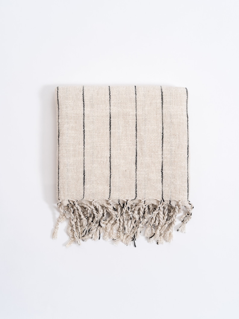 May include: A cream-colored striped throw blanket with black stripes and fringe on the bottom edge.