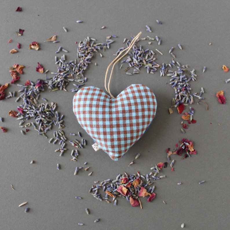 heart shaped organic lavender sachet, 3 inch tall, made out of upcycled cotton with light blue and brown gingham. Sachet has a twine loop for hanging, and is displayed with loose lavender and rose petals around it. front view.