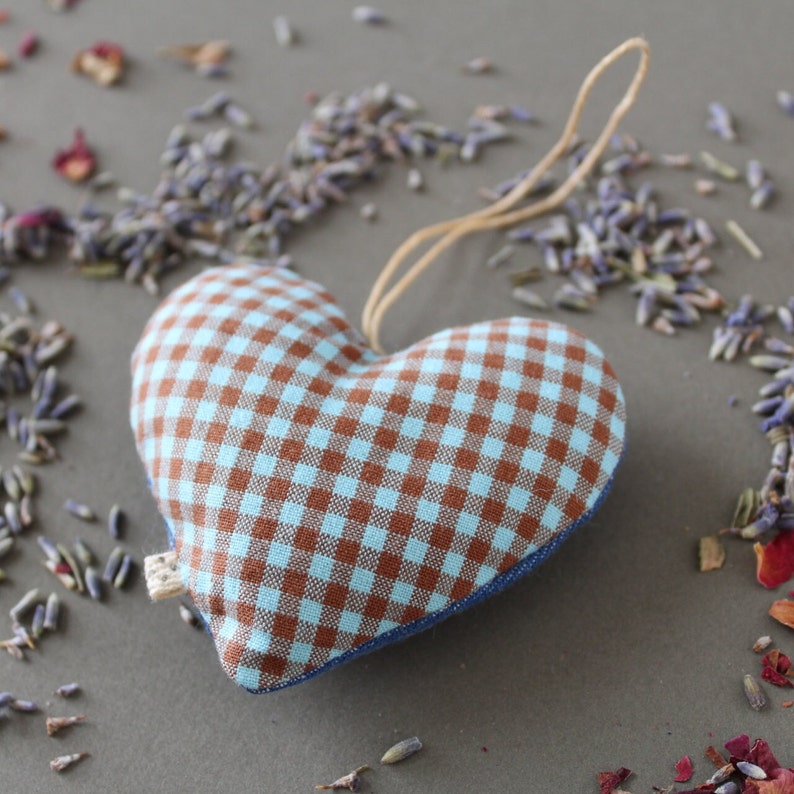 heart shaped organic lavender sachet, 3 inch tall, made out of upcycled cotton with light blue and brown gingham. Sachet has a twine loop for hanging, and is displayed with loose lavender and rose petals around it.