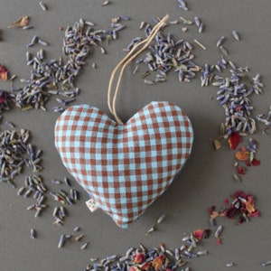 heart shaped organic lavender sachet, 3 inch tall, made out of upcycled cotton with light blue and brown gingham. Sachet has a twine loop for hanging, and is displayed with loose lavender and rose petals around it. close up view.