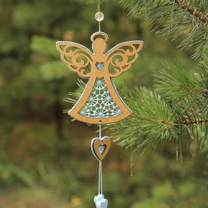 Op de afbeelding: Een houten engel ornament met een blauw-wit gepatroneerd jurkje en een hangende hart charme. Het ornament hangt aan een dennentak.