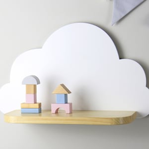 May include: White cloud-shaped shelf with a wooden shelf and colorful wooden blocks on top. The shelf is mounted on a white wall.