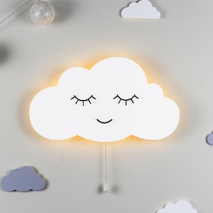 Könnte beinhalten: Ein weißes, wolkenförmiges Nachtlicht mit einem lächelnden Gesicht und geschlossenen Augen. Die Lampe hat eine Zugkette.