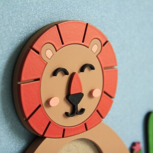 May include: A wooden lion with a red mane and a smiling face. The lion has a brown body and black eyes. The lion is holding a green cactus with pink flowers.