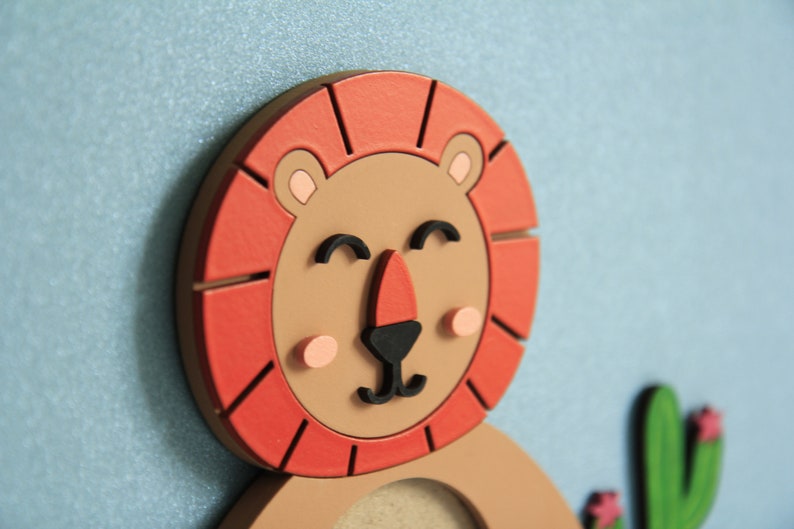 May include: A wooden lion with a red mane and a smiling face. The lion has a brown body and black eyes. The lion is holding a green cactus with pink flowers.