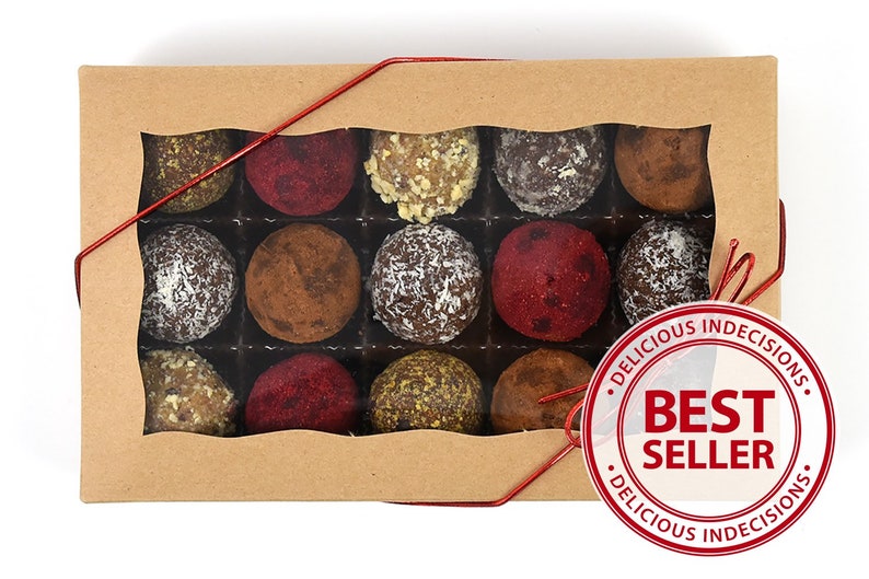 May include: A box of assorted chocolate truffles in a clear plastic container. The box is brown and has a red ribbon tied around it. The box is labeled "Delicious Indecisions" and "Best Seller".