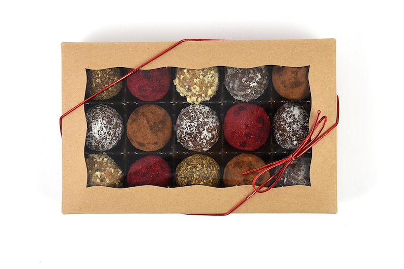 May include: A box of assorted chocolate truffles in a clear windowed box tied with a red ribbon. The truffles are arranged in a grid pattern and are various colors, including brown, white, and red.