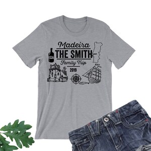 May include: A gray t-shirt with a black design that says "Madeira The Smith Family Trip 2019". The design also includes a bottle of port wine, a compass, a ship, and a castle.
