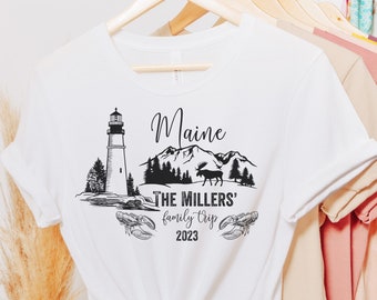May include: White t-shirt with a black graphic design featuring a lighthouse, mountains, a moose, and the text "Maine The Millers' family trip 2023".
