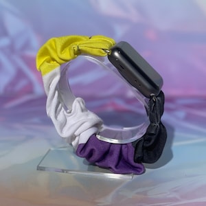 May include: A black, white, yellow and purple scrunchie watch band. The band is made of fabric and is designed to look like the asexual pride flag.