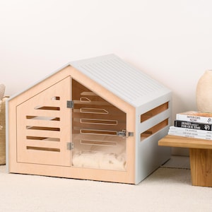 May include: A light gray and natural wood pet house with a gabled roof, featuring a front door with horizontal slats and a clear acrylic panel. The structure includes side ventilation slats and a metal latch on the door, with a soft white cushion inside.