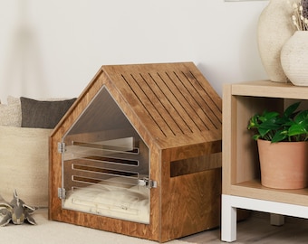 May include: A wooden dog house with a clear acrylic front door and roof slats. The house has a rectangular base and a pitched roof. A white cushion is visible inside the house. The dog house is placed on a cream-colored rug.