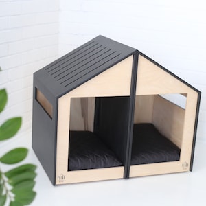 K&ouml;nnte beinhalten: Ein modernes Hundehaus aus Holz und Schwarz mit zwei separaten Abteilen, jedes mit einem schwarzen Kissen. Das Haus hat ein schlichtes, minimalistisches Design und ist perfekt f&uuml;r zwei Hunde.
