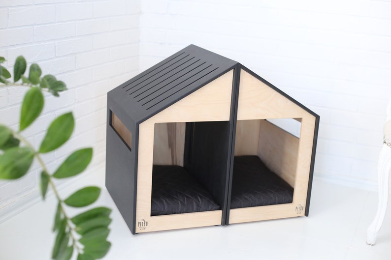 K&ouml;nnte beinhalten: Ein modernes Hundehaus aus Holz und Schwarz mit zwei separaten Abteilen, jedes mit einem schwarzen Kissen. Das Haus hat ein schlichtes, minimalistisches Design und ist perfekt f&uuml;r zwei Hunde.