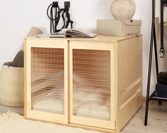 May include: A light wood dog crate with sliding doors and a white cushion inside. The crate is sitting on a light brown rug.