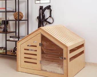 May include: A light wood dog house with a sloped roof and a clear plastic door. The house has a small bed inside and is sitting on a light brown carpet.