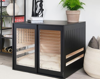 Könnte beinhalten: Eine schwarze Hundebox mit Schiebetüren und Lamellendesign. Die Kiste hat transparente Paneele und einen Holzinnenraum. Eine Topfpflanze steht auf der Kiste. Vor der Kiste liegt ein weißer Teppich.