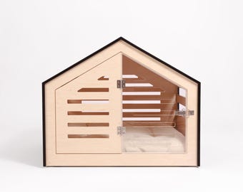 May include: A wooden dog house with a black trim and a clear plastic door. The house has a white cushion inside.