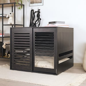 Könnte beinhalten: Eine schwarze Hundebox aus Holz mit Schiebetür und Lamellendesign. Die Box hat eine rechteckige Form und ein weiches, weißes Kissen ist im Inneren sichtbar. Die Box steht auf einem weißen Teppich.