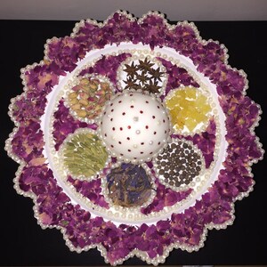 May include: A white plate with a pearl border is filled with various spices and dried flowers. The center of the plate features a white sphere with red polka dots.