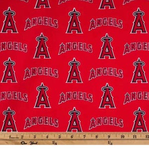 May include: Red fabric with a repeating pattern of the Los Angeles Angels baseball team logo. The logo features a stylized "A" with a halo and the word "ANGELS" in white. A ruler is at the bottom, measuring up to 12 inches.
