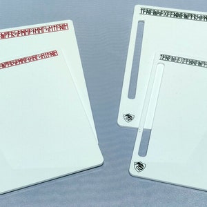 Könnte beinhalten: Zwei weiße Kunststoff-Schneidebretter mit einem Schlitz für ein Messer. Das obere Brett hat roten Text, der "TENNEFNE EXFFENME FRFMMF HMME MTTFM" lautet, und das untere Brett hat schwarzen Text, der "TENNEFNE EXFFENME FRFMMF HMME MTTFM" lautet.