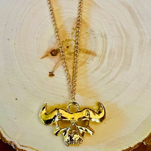 May include: A gold chain necklace with a skull pendant. The skull has horns and a detailed design.