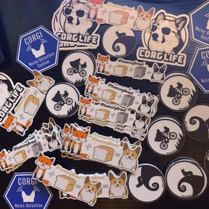 Puede incluir: Una colecci&oacute;n de pegatinas coloridas con un perro corgi, un zorro, una tostadora, pan y una silueta de un personaje de la pel&iacute;cula 'E.T. el extraterrestre'. Las pegatinas tienen el texto 'Corgi Life' y '@teamcorgibrand' en ellas.