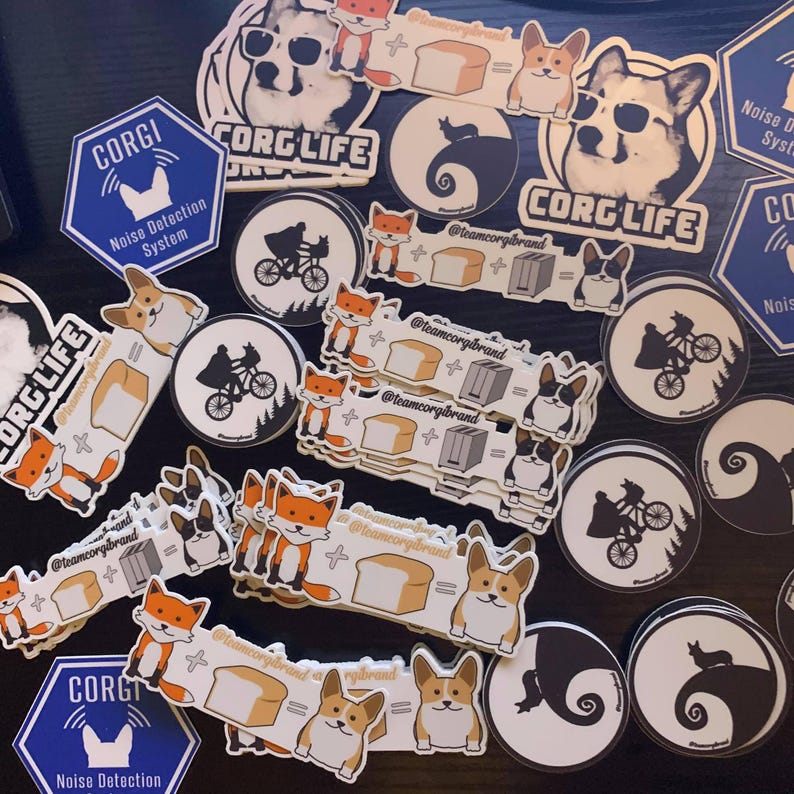 Puede incluir: Una colecci&oacute;n de pegatinas coloridas con un perro corgi, un zorro, una tostadora, pan y una silueta de un personaje de la pel&iacute;cula 'E.T. el extraterrestre'. Las pegatinas tienen el texto 'Corgi Life' y '@teamcorgibrand' en ellas.