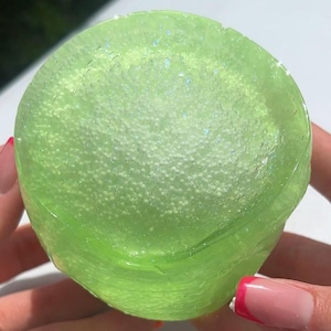 K&ouml;nnte beinhalten: Nahaufnahme eines durchscheinenden, limettengr&uuml;nen Schleimballs. Der Schleim ist mit kleinen, wei&szlig;en, kugelf&ouml;rmigen K&uuml;gelchen gef&uuml;llt. Der Schleim hat ein gl&auml;nzendes Aussehen und ist leicht irisierend. Das Bild ist gut beleuchtet und hebt die Textur und Farbe des Schleims hervor.