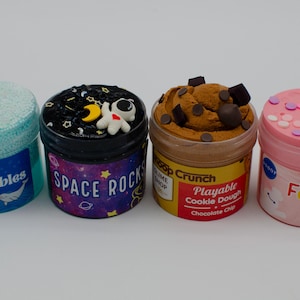 May include: Four colorful slime containers. One is light blue with "Lava Bubbles" text, another is black with a space theme and "Space Rocks" text, the third is brown with "Playable Cookie Dough" text, and the last is pink with "Funfeti" text.