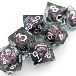 Könnte beinhalten: Satz von acht transparenten Würfeln mit schwarzen und violetten Akzenten. Jeder Würfel zeigt eine andere Zahl von 1 bis 8 sowie eine Grafik einer Kreatur mit Augen und Zähnen.
