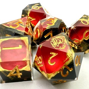 May include: Set of seven polyhedral dice with a red and black design. The dice have gold-colored numbers and accents. The dice are made of a clear resin material.